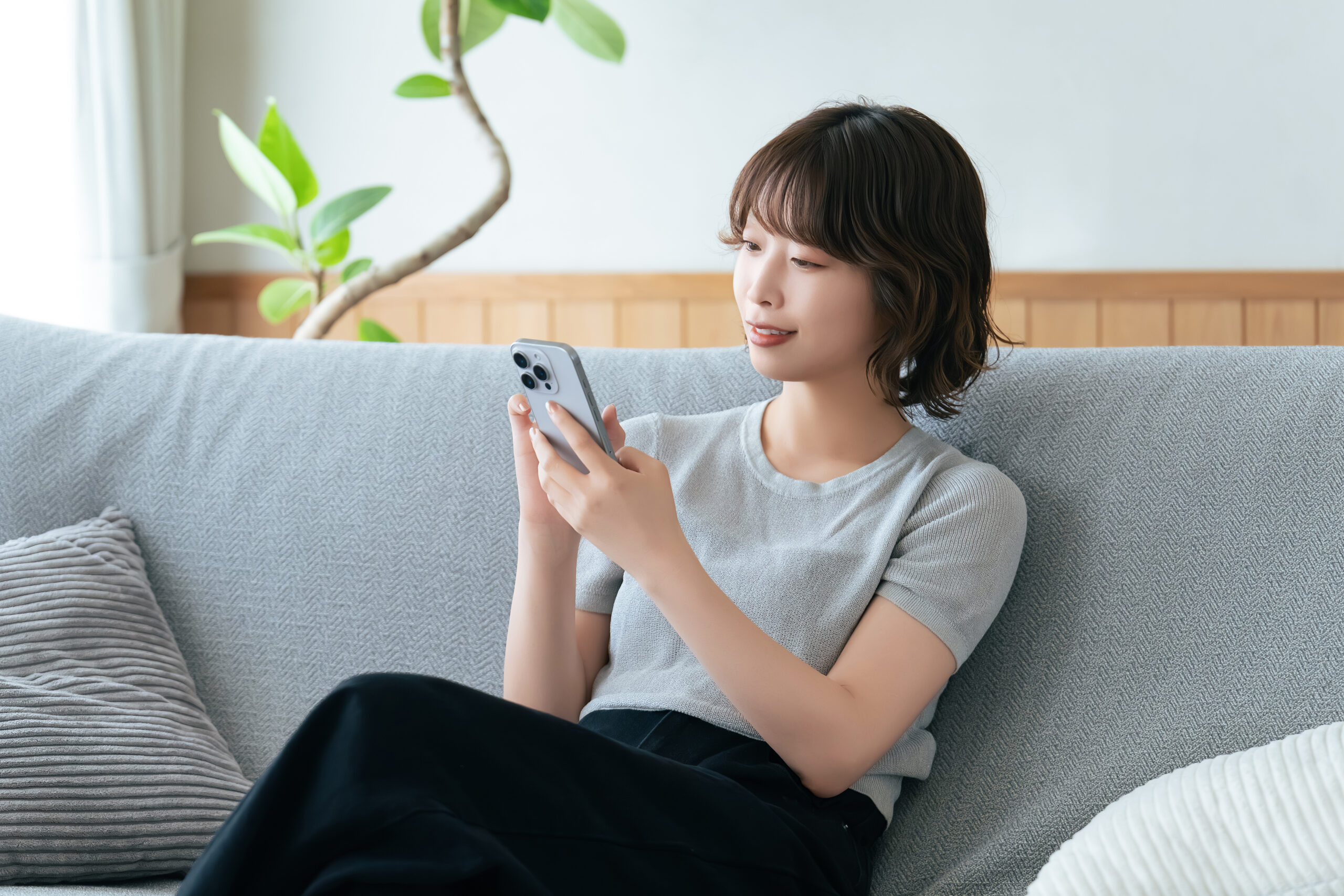 ソファに座ってスマホを使う笑顔の女性